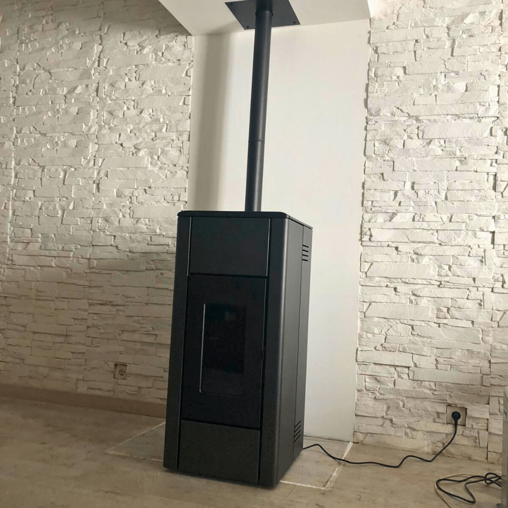 Gros plan sur un poêle à granulés noir installé devant un mur en pierres blanches, avec prise électrique visible, rénovation énergétique d’un logement en Hauts-de-France.