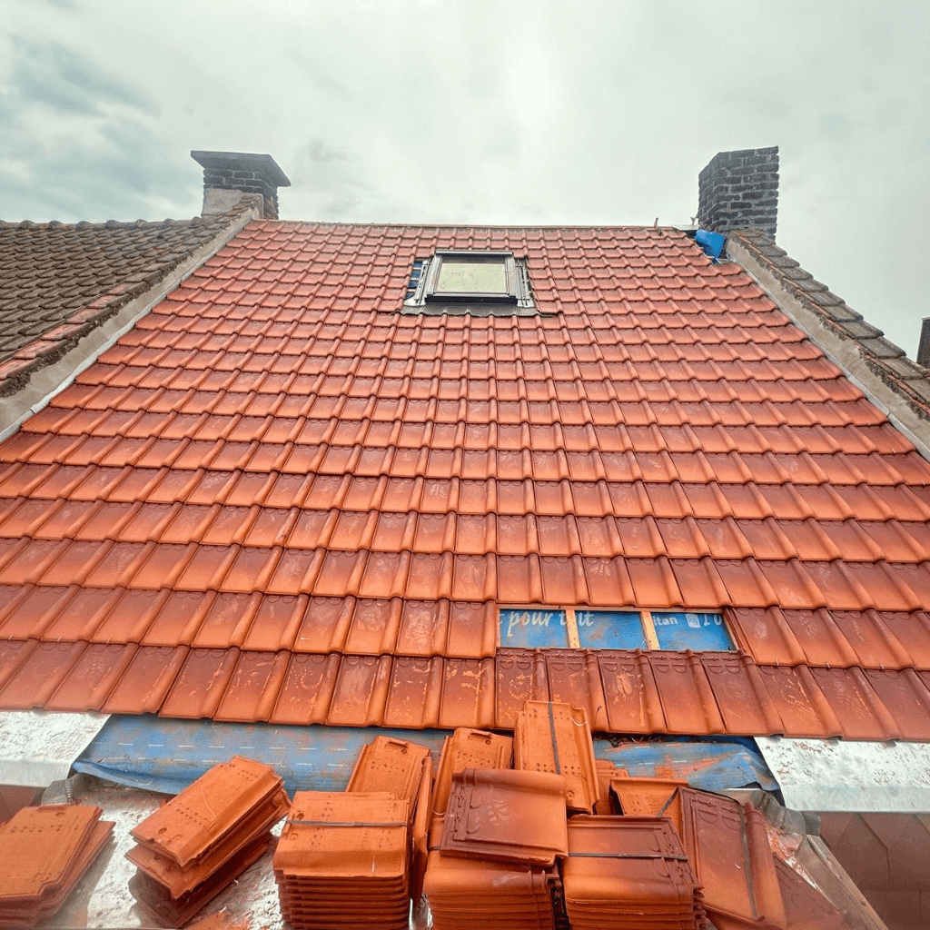 Toit en rénovation à Tourcoing : artisan RGE posant des tuiles terre cuite neuves autour d’une fenêtre de toit Velux.