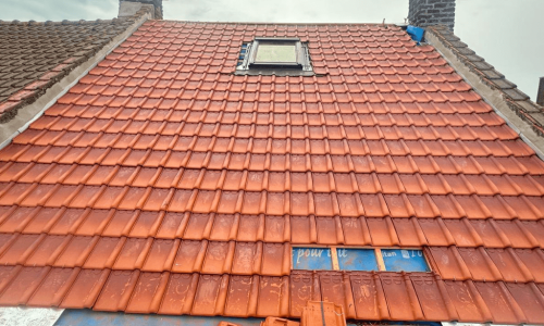 Rénovation de toiture à Tourcoing : pose de tuiles terre cuite autour d’une fenêtre de toit – Artisan RGE Toit en rénovation à Tourcoing : artisan RGE posant des tuiles terre cuite neuves autour d’une fenêtre de toit Velux.