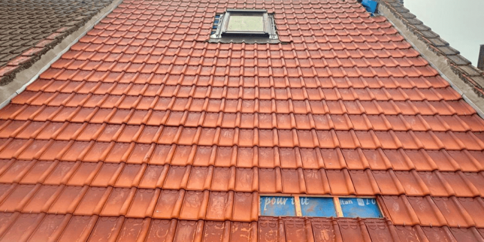 Rénovation de toiture à Tourcoing : pose de tuiles terre cuite autour d’une fenêtre de toit – Artisan RGE Toit en rénovation à Tourcoing : artisan RGE posant des tuiles terre cuite neuves autour d’une fenêtre de toit Velux.